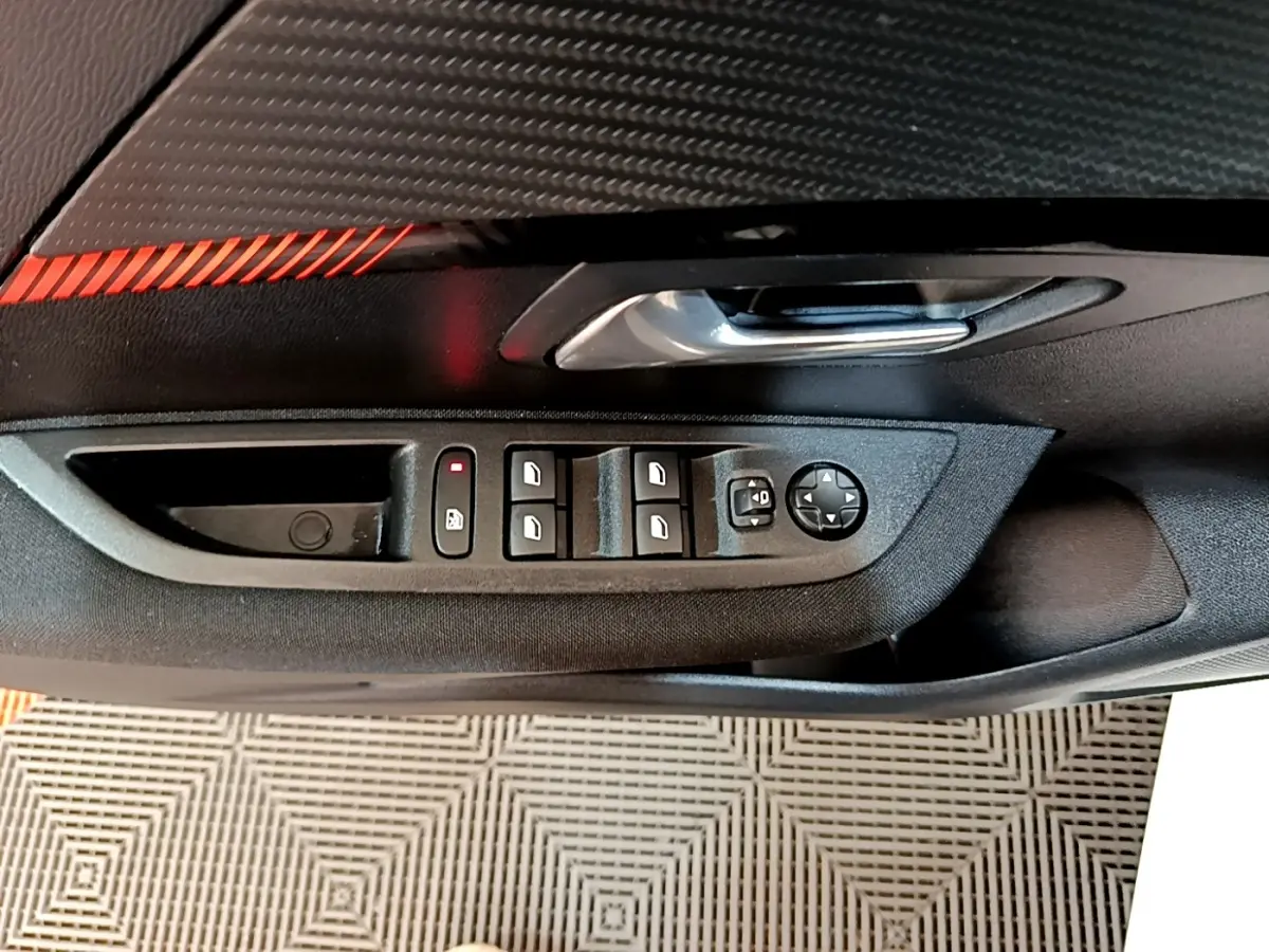 Vue rapprochée de la portière côté conducteur du Peugeot 208 électrique blanc, avec commandes des vitres et rétroviseurs.