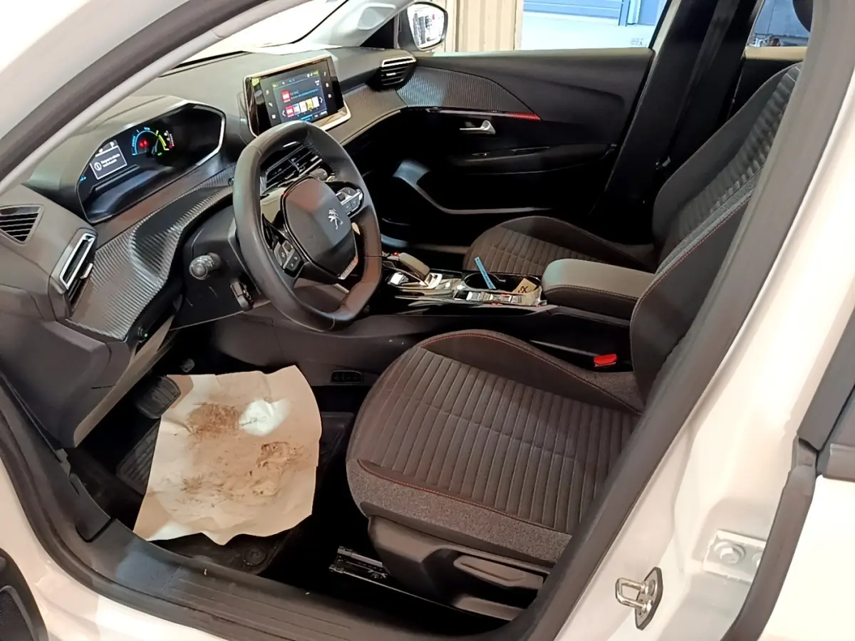 Intérieur avant droit d'une Peugeot 208 électrique blanche 2022, tableau de bord avec écran tactile et sièges tissu noirs.