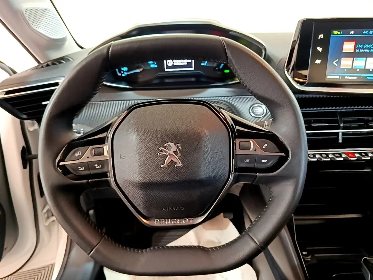 Vue intérieure centrée sur le volant cuir multifonctions d’une Peugeot 208 électrique blanche avec tableau de bord digital.