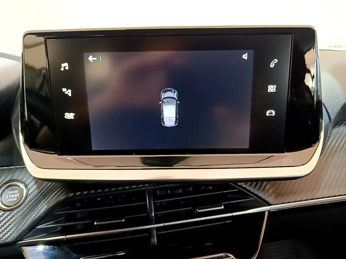 Écran tactile central affichant la vue de dessus du véhicule, tableau de bord noir avec finition carbone dans une Peugeot 208 électrique.