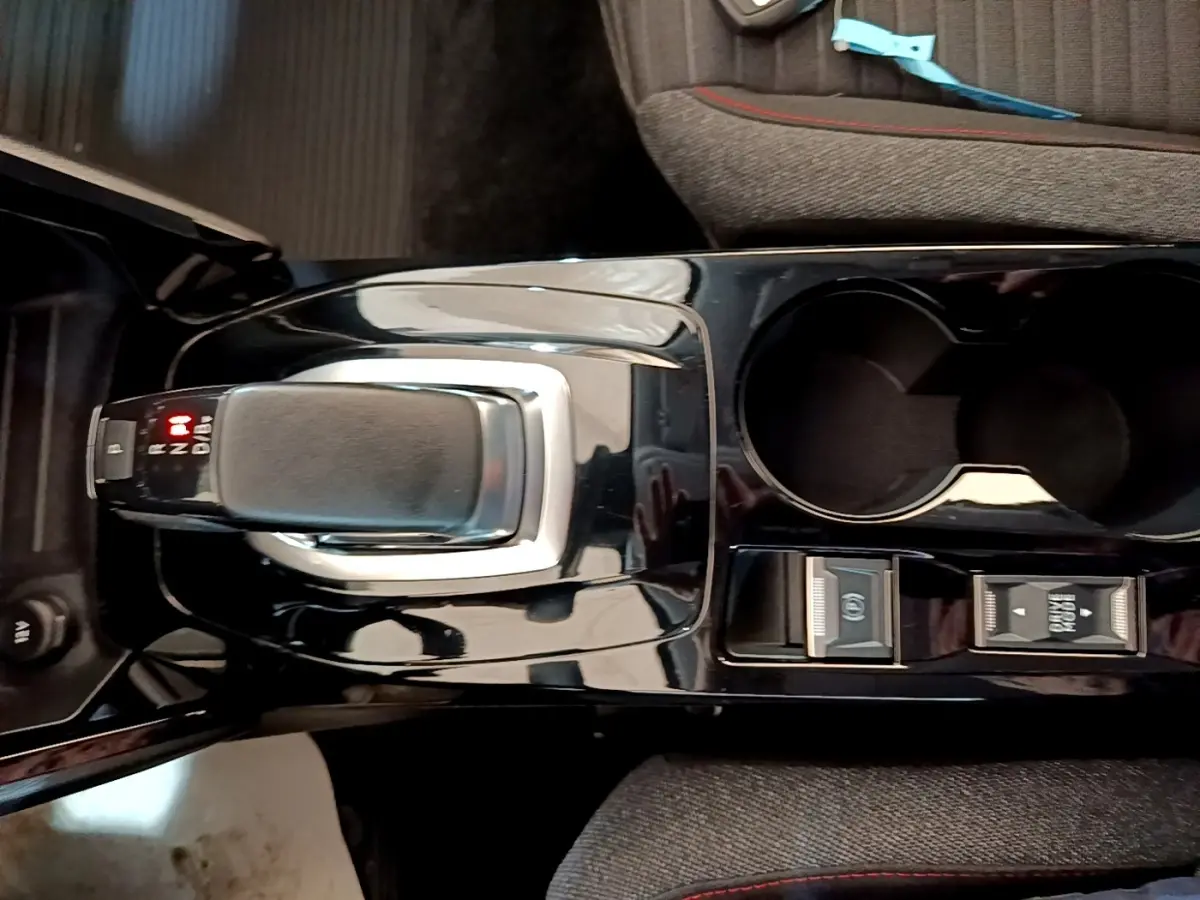 Vue plongeante sur la console centrale noire de la Peugeot 208 électrique avec levier de vitesse automatique et porte-gobelets.