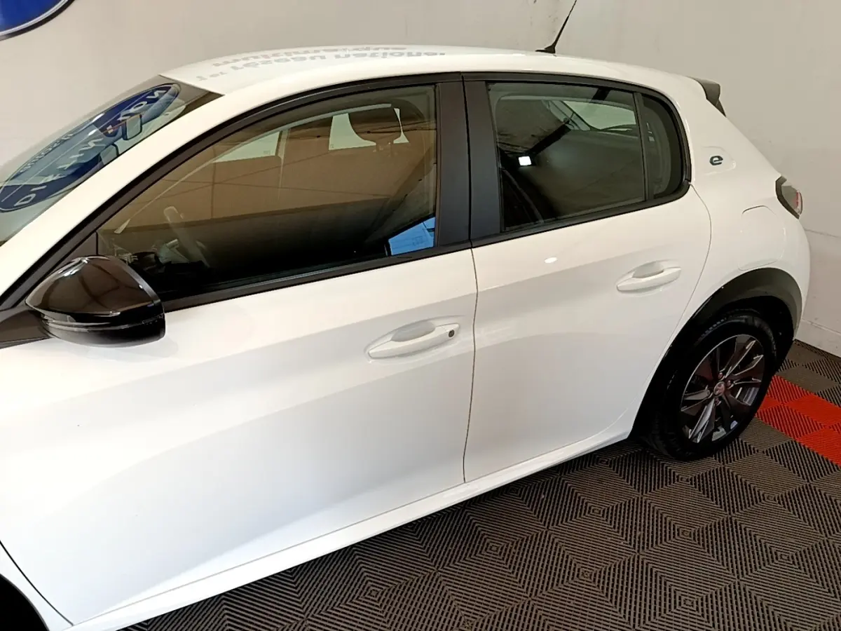 Profil côté gauche d'une Peugeot 208 électrique blanche avec rétroviseur noir et jantes alliage foncé.