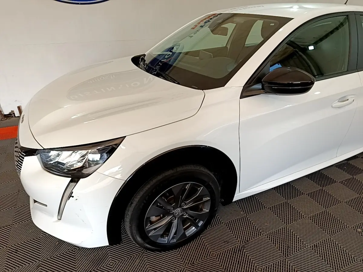 Vue 3/4 avant droit d'une Peugeot 208 électrique blanche avec rétroviseur noir et jante foncée.