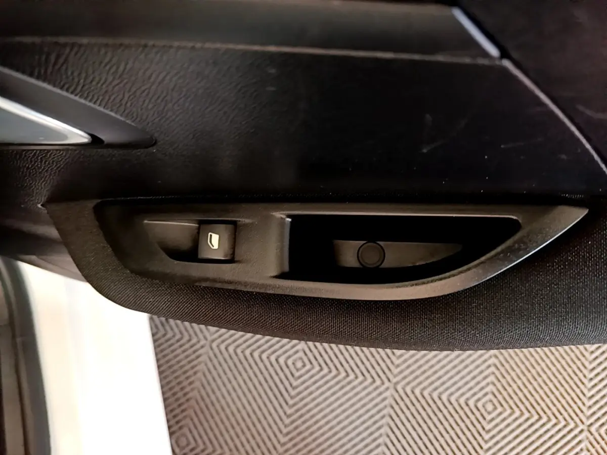 Gros plan sur la commande de lève-vitre électrique côté conducteur de la Peugeot 208 électrique blanche, intérieur noir.