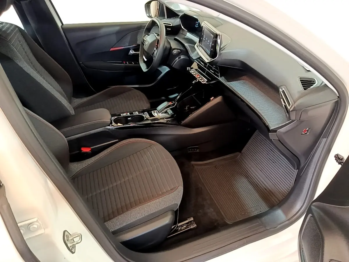 Vue intérieure côté passager de la Peugeot 208 électrique blanche, avec tableau de bord moderne et sièges noirs.