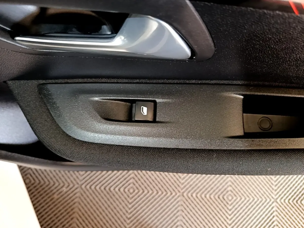 Gros plan sur la commande de lève-vitre côté conducteur dans la porte intérieure noire d’une Peugeot 208 électrique blanche.