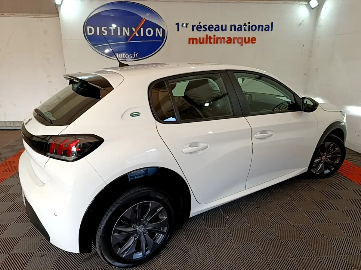 Peugeot 208 électrique blanche vue 3/4 arrière droit, avec jantes foncées et logo "e" vert sur l'aile arrière.