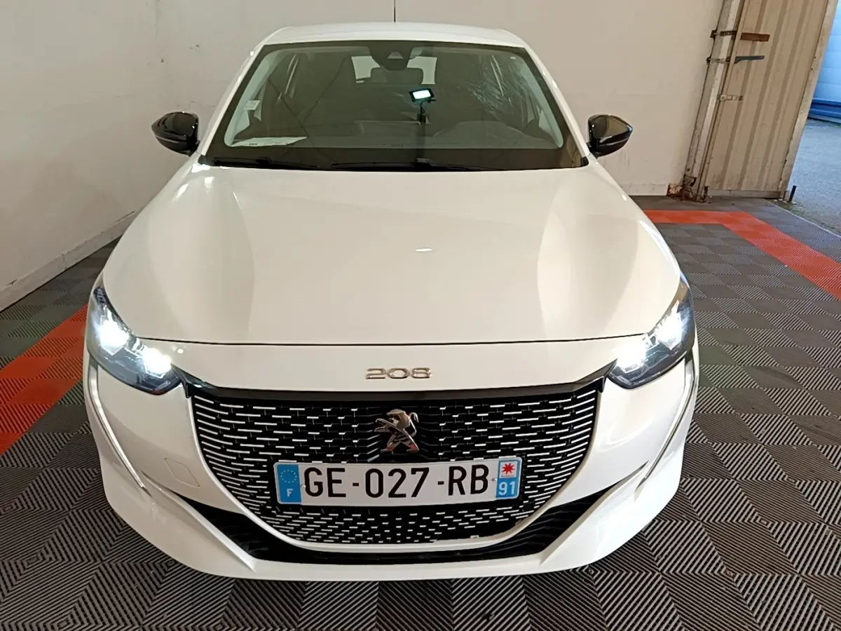 Vue avant d'une Peugeot 208 électrique blanche avec phares allumés et calandre noire distinctive.