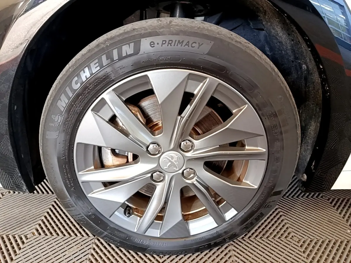 Gros plan sur la roue avant gauche d’une Peugeot 208 électrique blanche, jante alliage avec logo lion au centre.