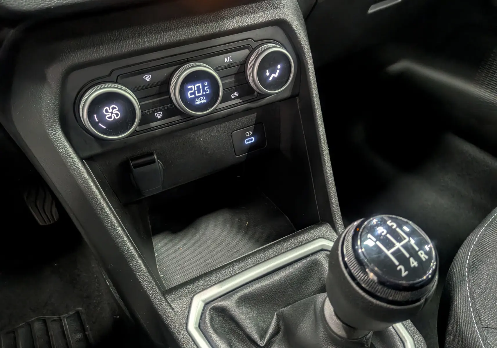 Gros plan sur la console centrale de la Dacia Sandero TCe 90 gris schiste, avec la commande de climatisation et levier de vitesse manuel.