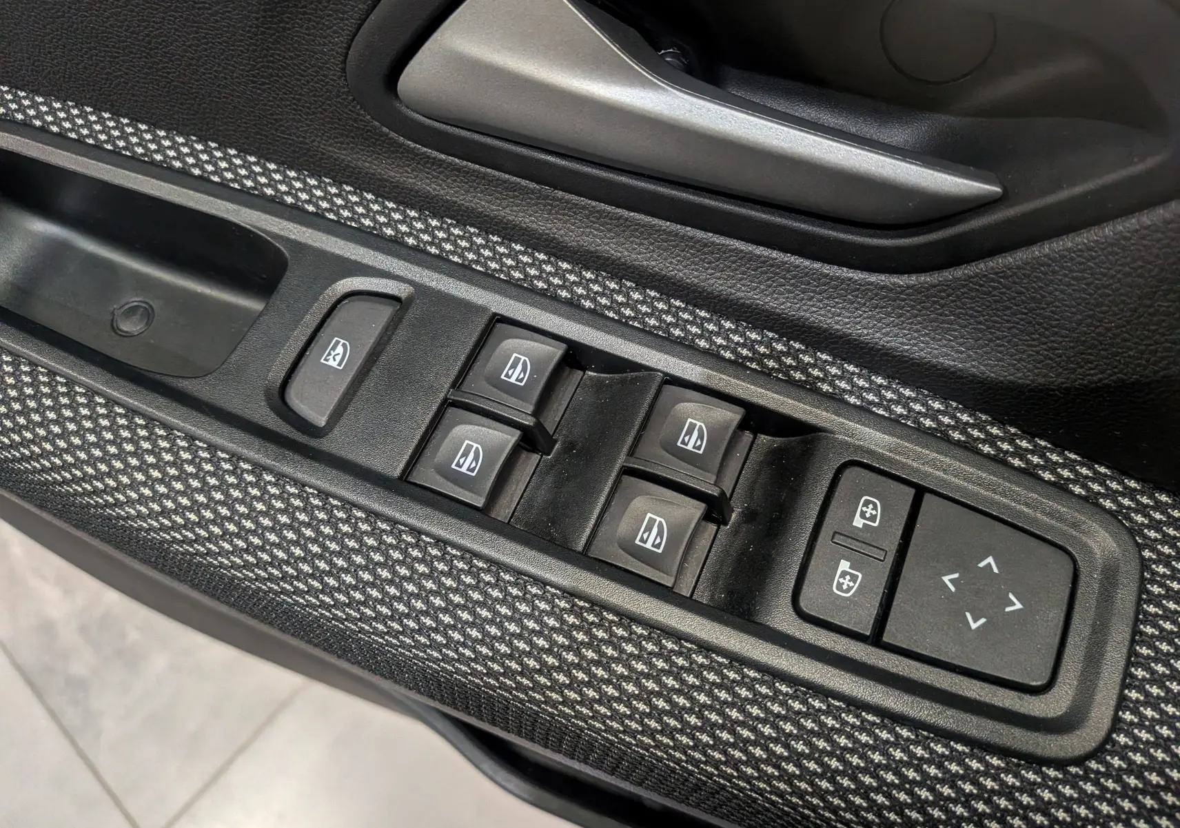 Gros plan sur les commandes des vitres électriques et rétroviseurs sur la portière côté gauche de la Dacia Sandero TCe 90 Gris Schiste 2025.