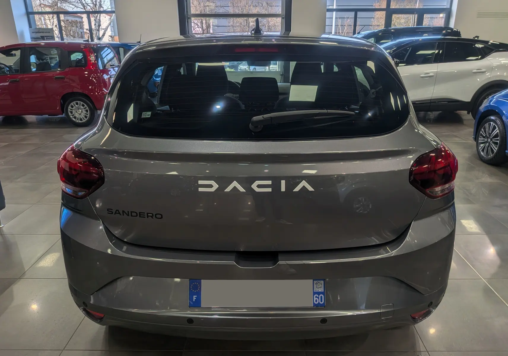 Vue arrière d'une Dacia Sandero TCe 90 CH JOURNEY gris schiste 2025 en showroom avec feux arrière rouges et lunette arrière dégagée.