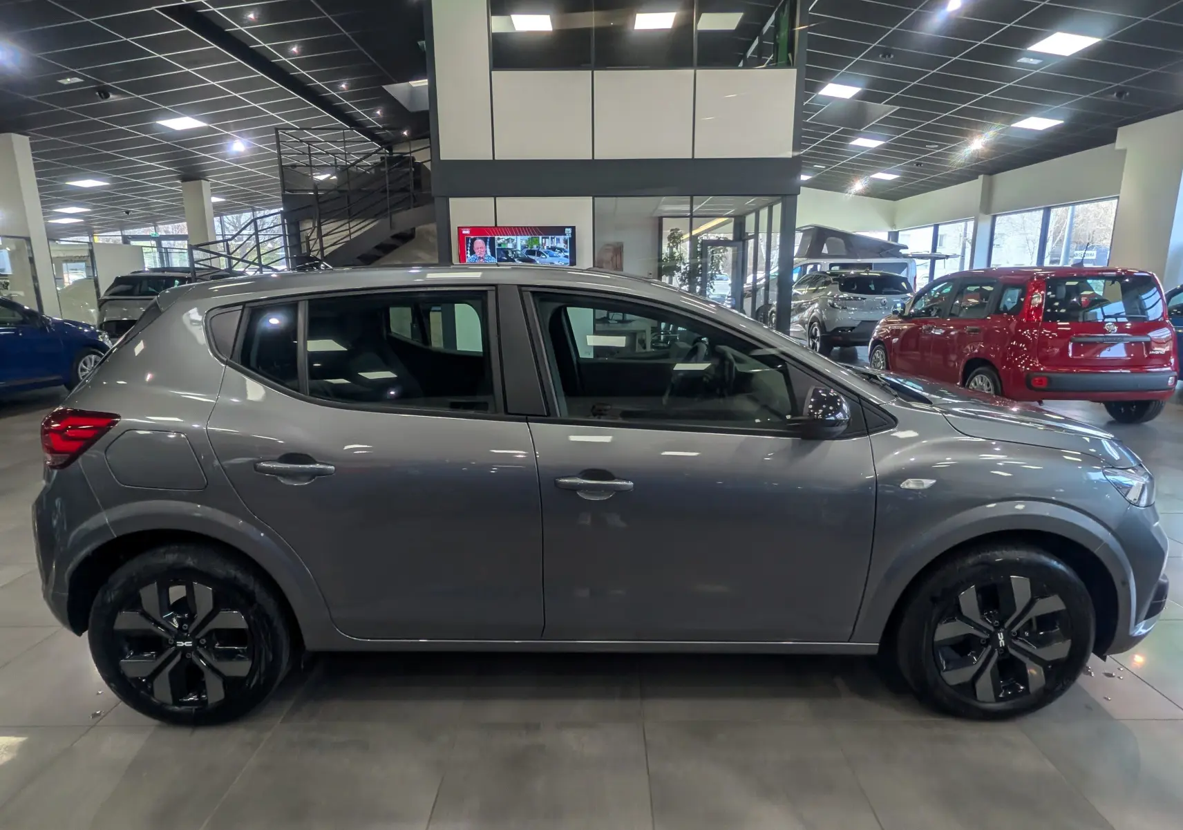 Profil côté droit d'une Dacia Sandero TCe 90 CH Journey 2025 en gris schiste, exposée en showroom lumineux.