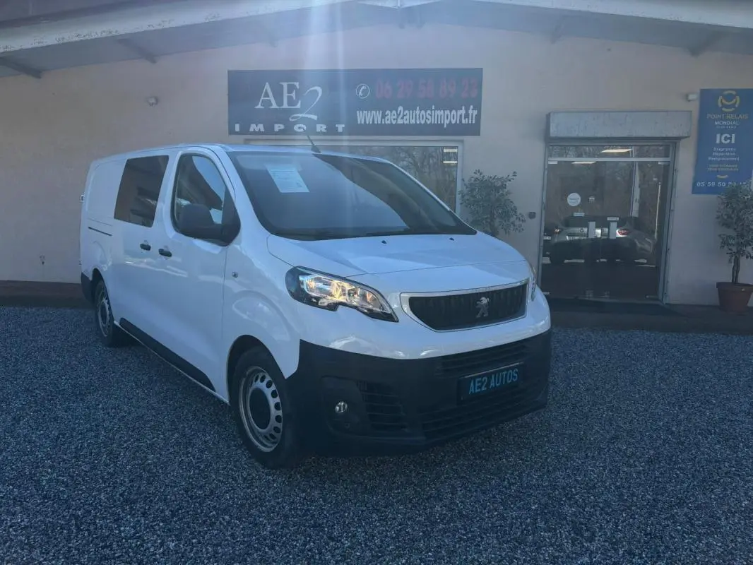 Peugeot Expert Fourgon blanc vu en 3/4 avant droit, avec calandre noire et jantes tôles, stationné devant un garage.