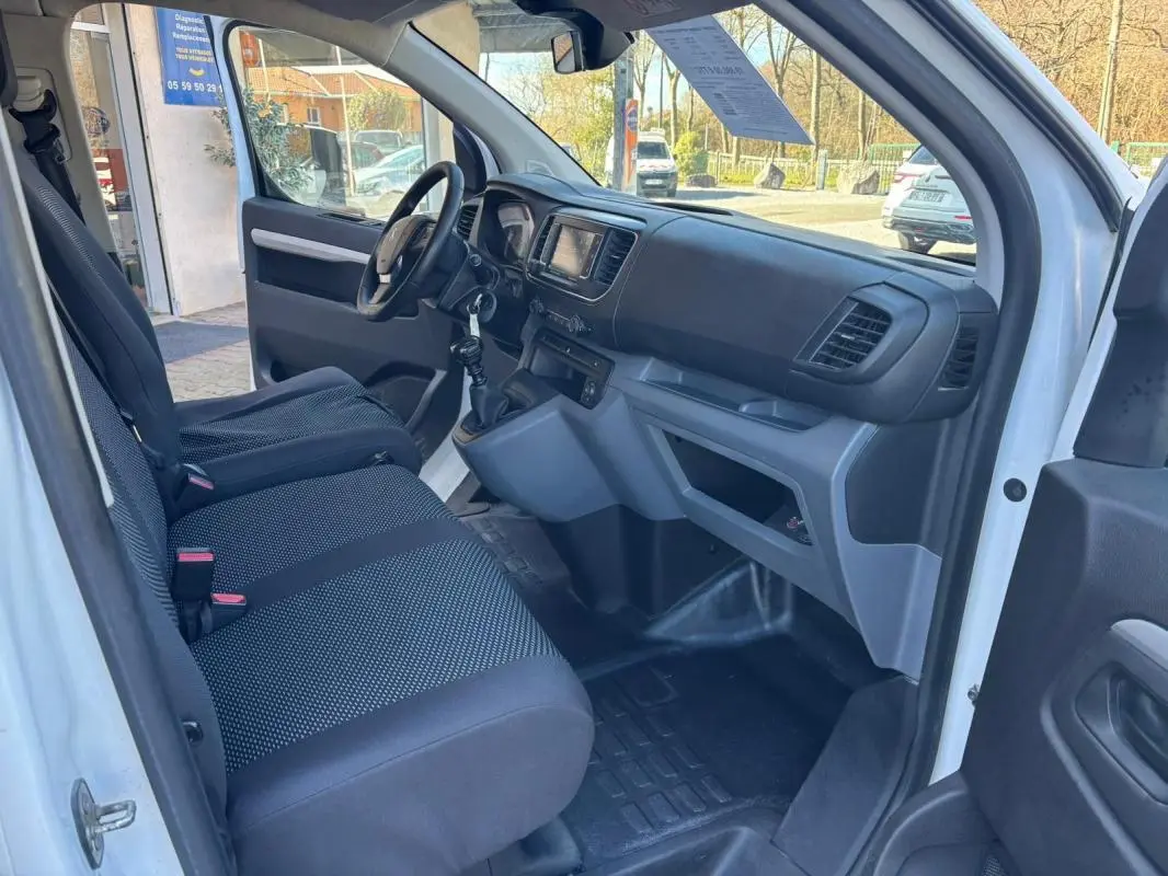 Vue intérieure côté conducteur du Peugeot Expert Fourgon blanc de 2018, montrant le tableau de bord et les sièges noirs.