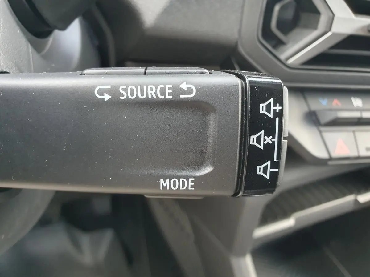 Gros plan sur la commande au volant du Dacia Duster 2026 gris schiste, avec boutons source et mode visibles.