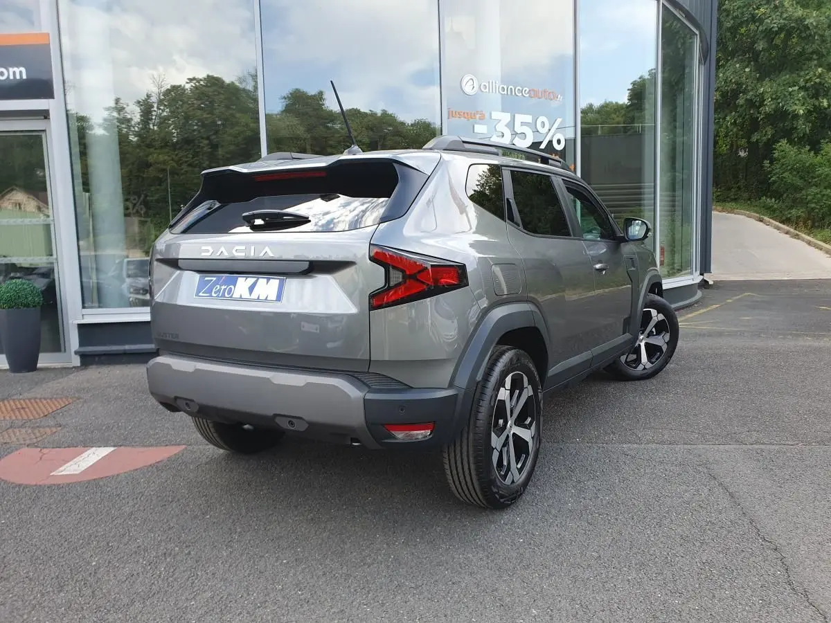 Vue 3/4 arrière droite du Dacia Duster gris schiste métallisé avec jantes alliage et barres de toit fixes.
