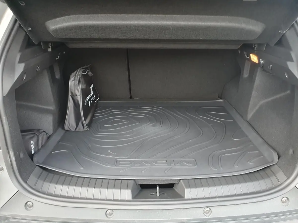 Coffre ouvert du Dacia Duster gris schiste 2026, vue intérieure montrant tapis de coffre et sac de secours noir.