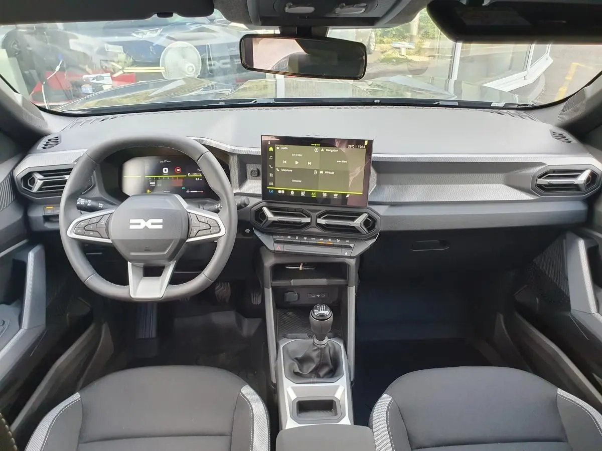 Vue intérieure frontale du tableau de bord du Dacia Duster 2026 avec écran tactile central et volant multifonction noir.