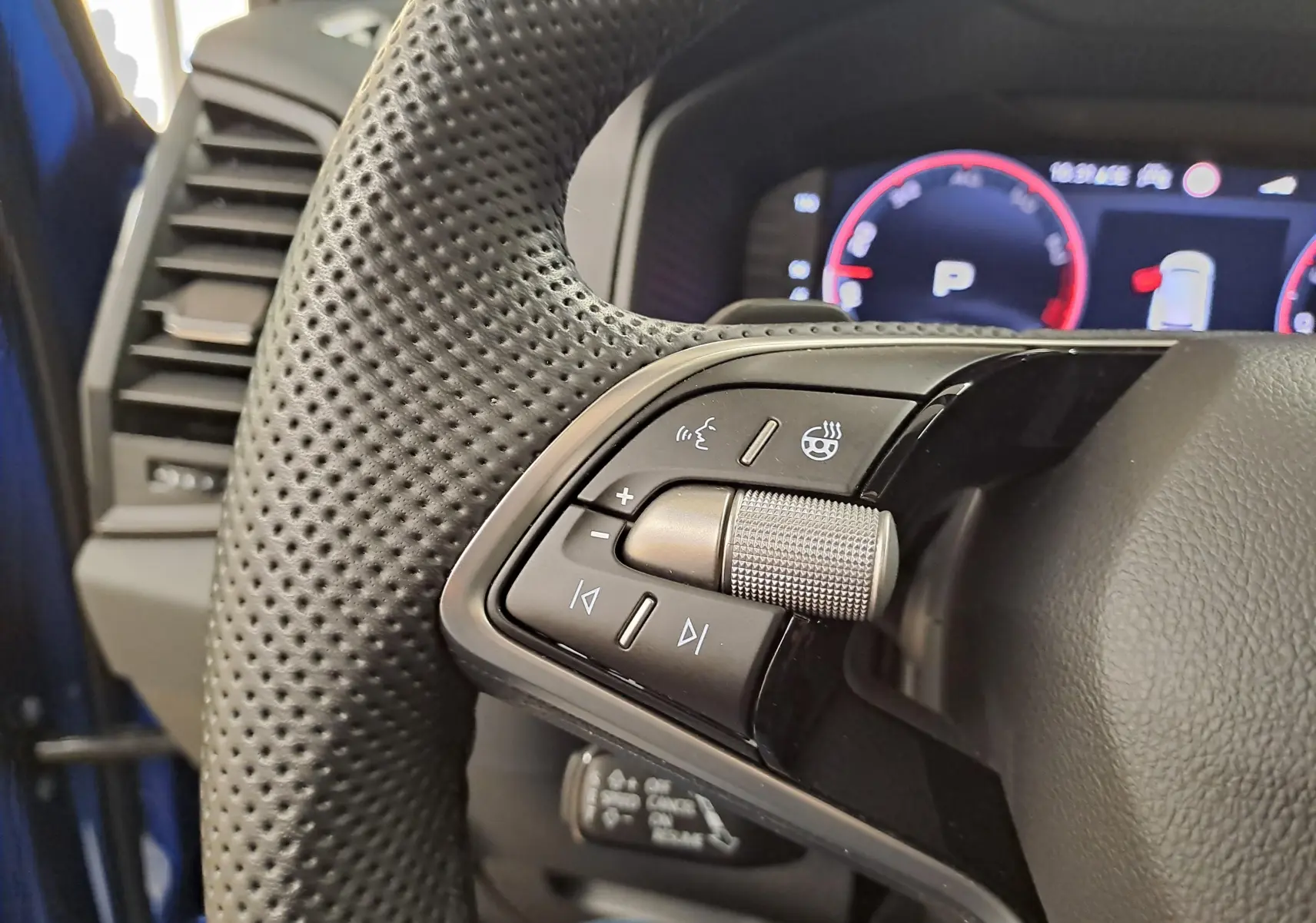 Gros plan sur les commandes gauche du volant perforé d’un Skoda Karoq Bleu RS 2025 avec tableau de bord numérique en arrière-plan.