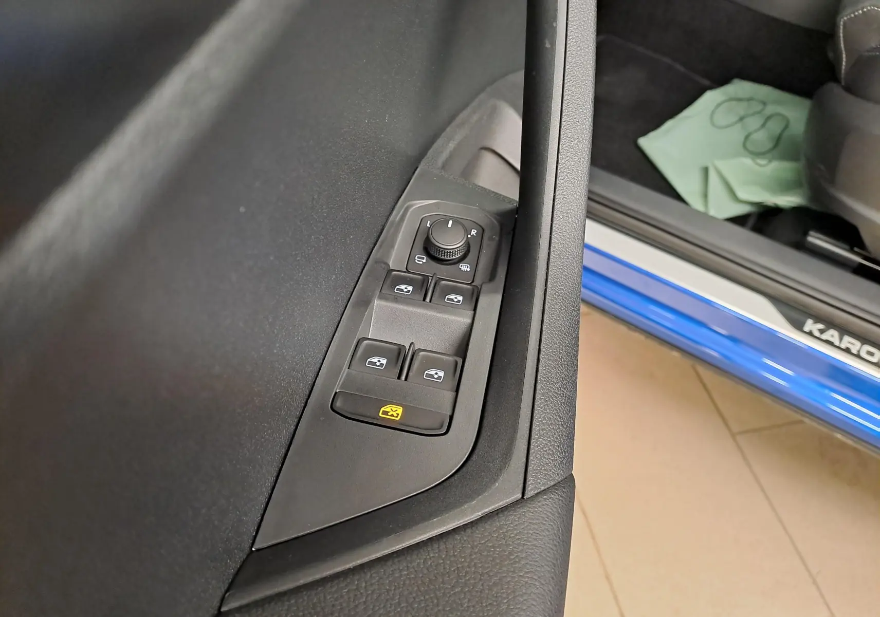Gros plan sur les commandes de vitres et rétroviseurs côté conducteur du Skoda Karoq Bleu RS avec seuil de porte visible.