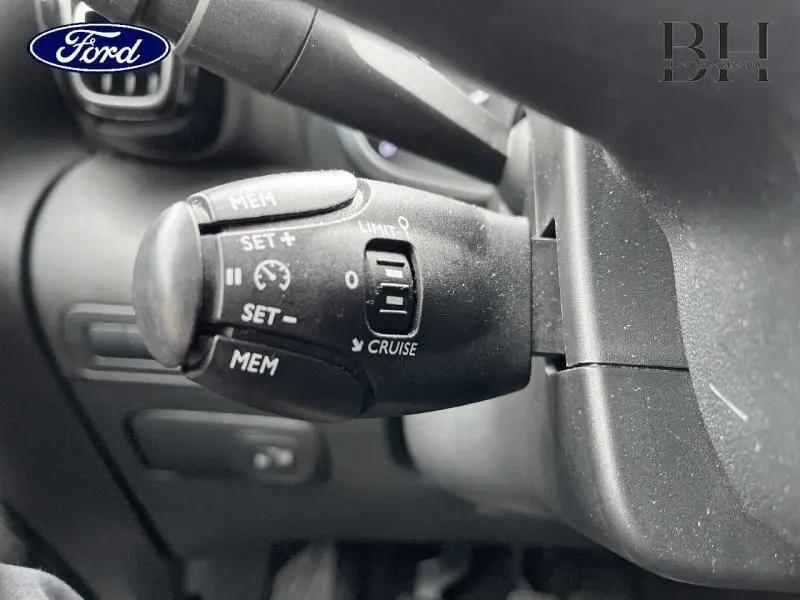 Gros plan sur la commande de régulateur de vitesse noire à gauche du volant dans l'habitacle d'une Citroën C3 Aircross blanche.