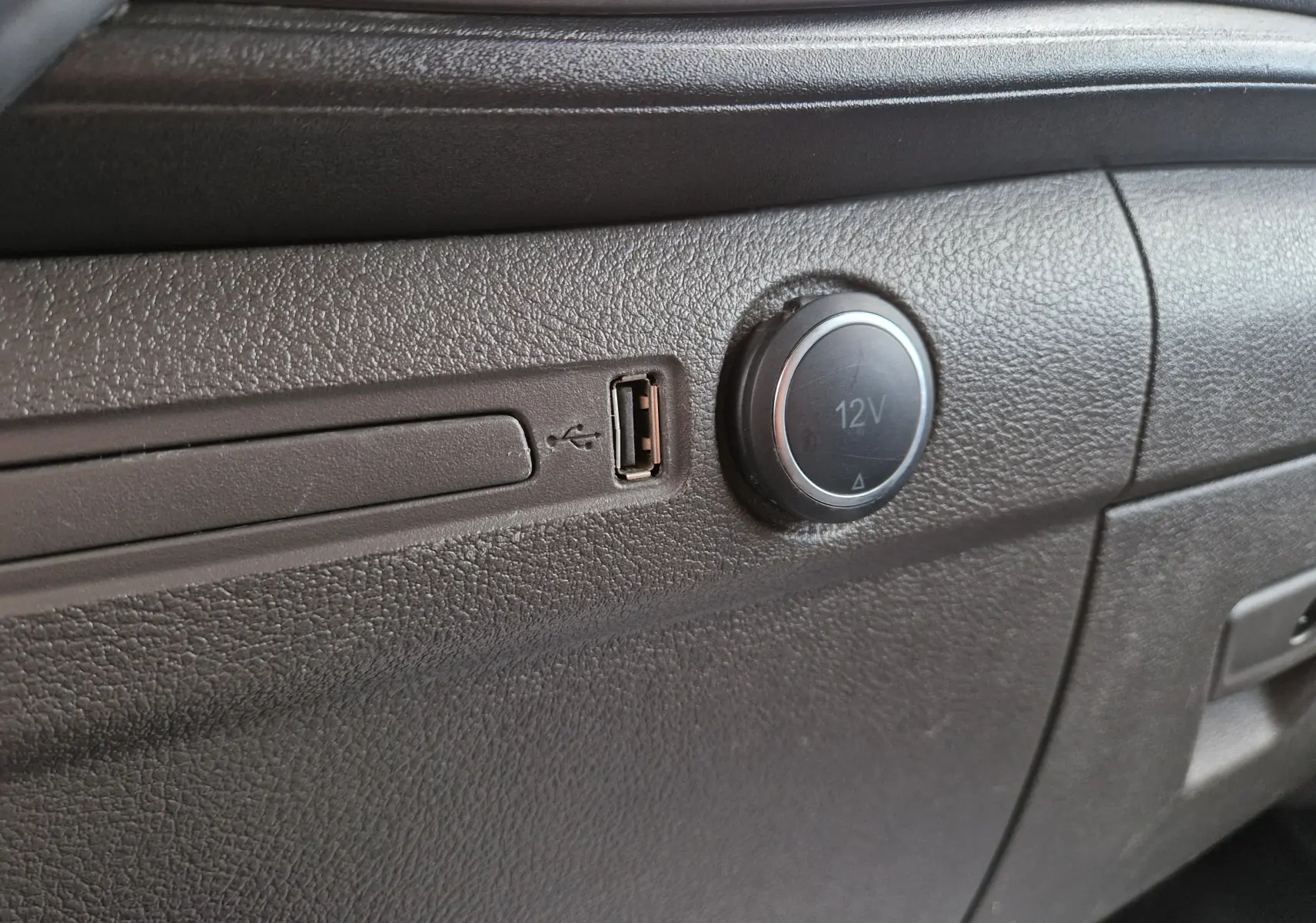 Détail intérieur montrant une prise USB et une prise 12V sur la planche de bord noire du Ford Transit Custom Fourgon.