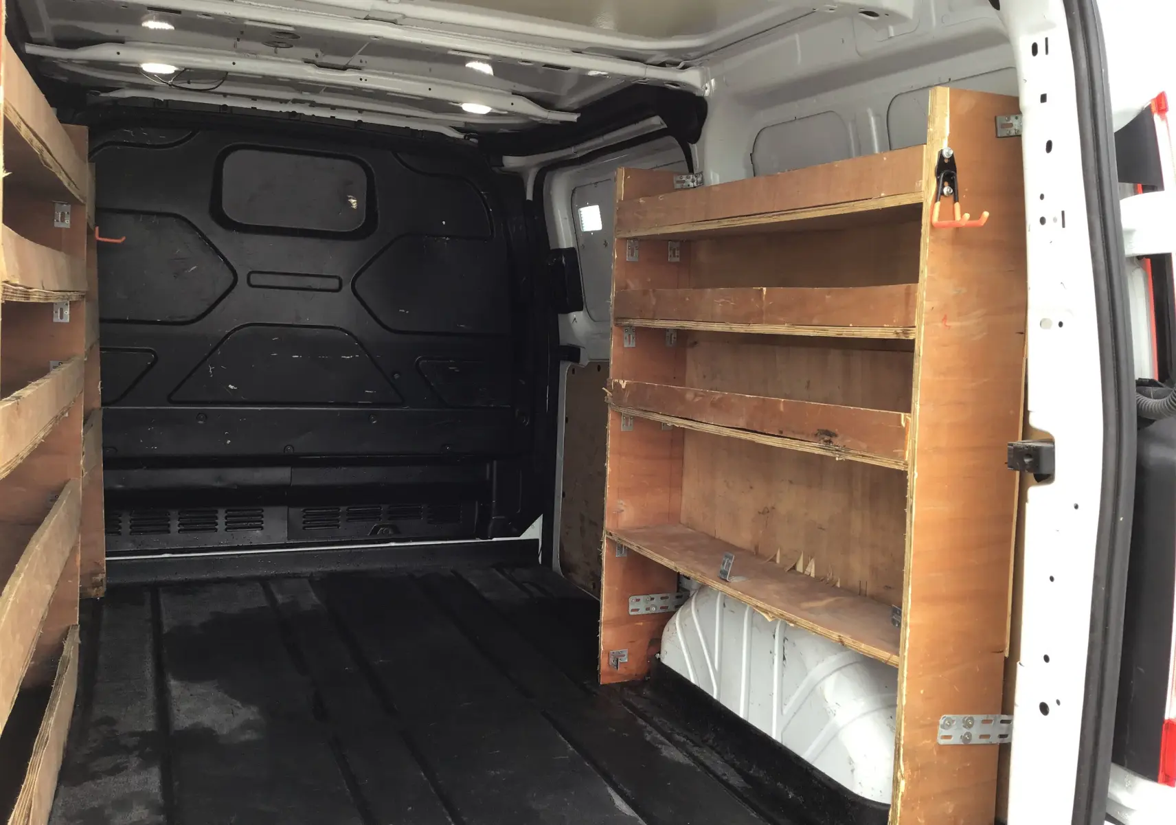 Vue intérieure arrière droite d’un Ford Transit Custom blanc 2021 avec étagères en bois intégrées dans le fourgon.