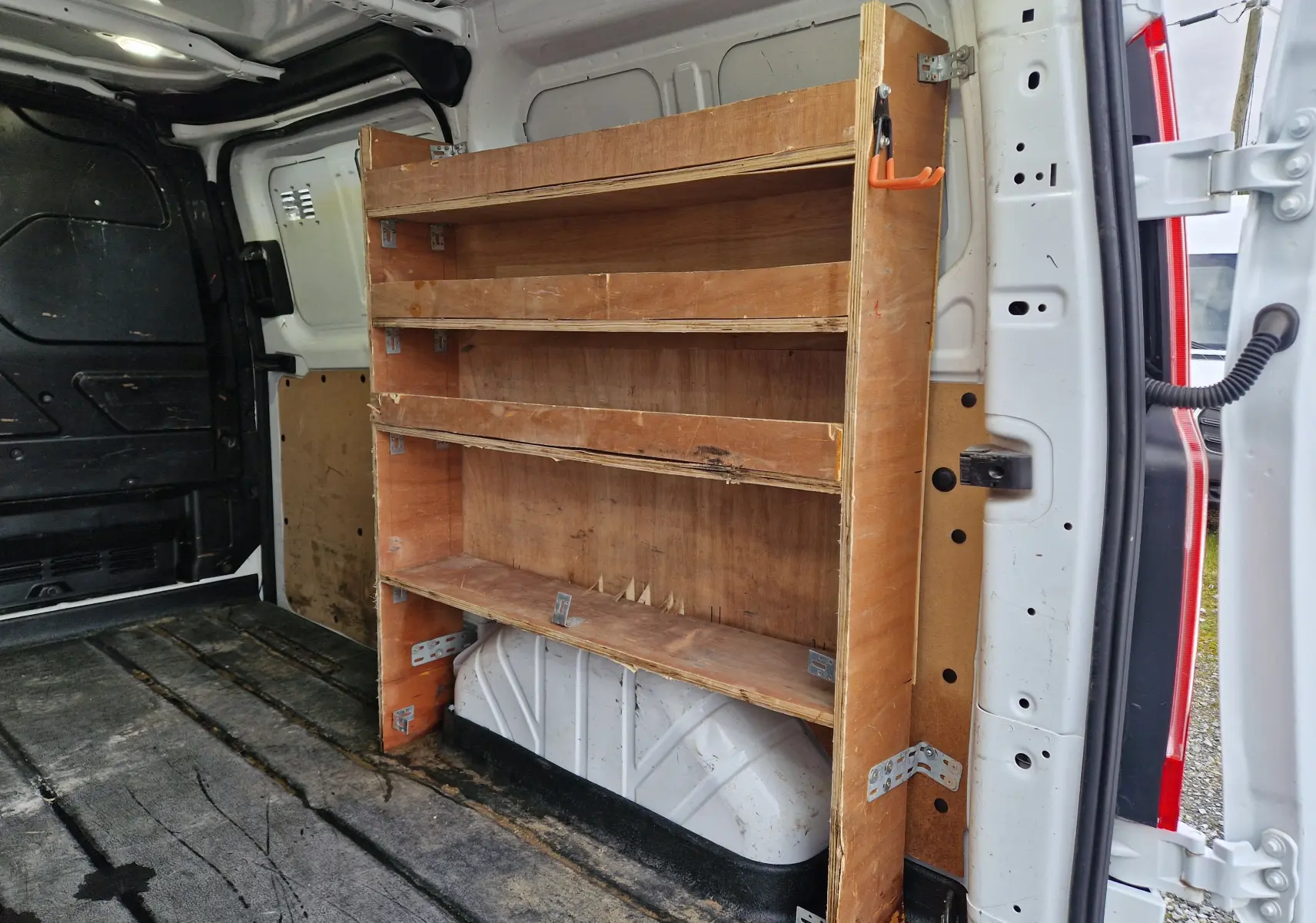 Vue de profil côté gauche d'un Ford Transit Custom blanc avec porte latérale coulissante ouverte révélant l'intérieur aménagé en bois.