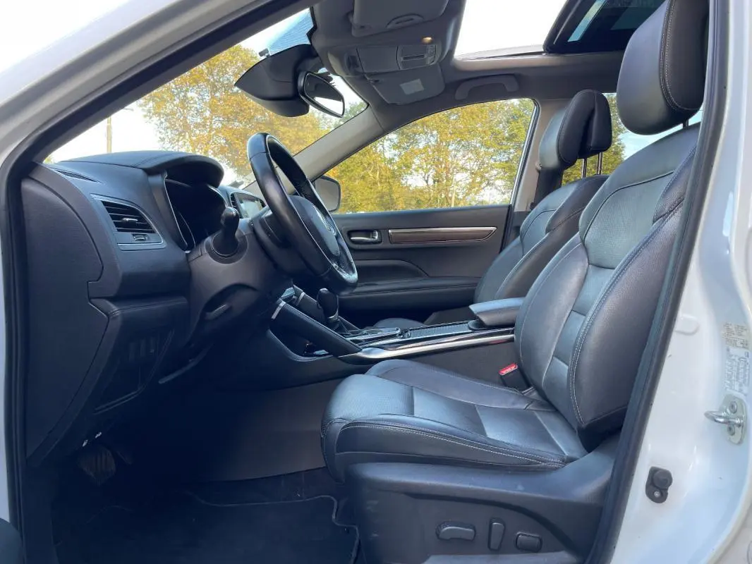 Vue intérieure côté conducteur du Renault Koleos blanc 2019 avec sièges cuir noirs et toit ouvrant panoramique visible.