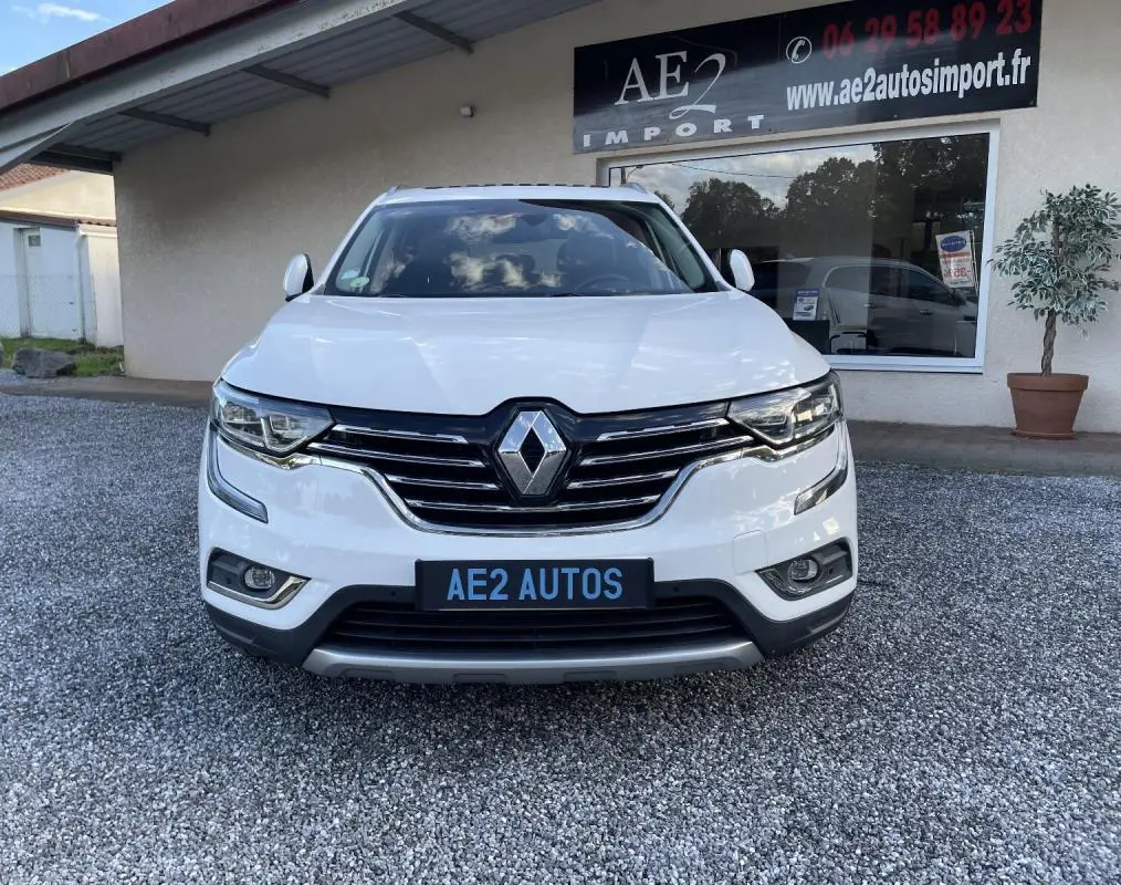 Vue frontale d’un Renault Koleos blanc 2019 avec calandre chromée et phares LED, stationné devant un garage AE2 Autos.