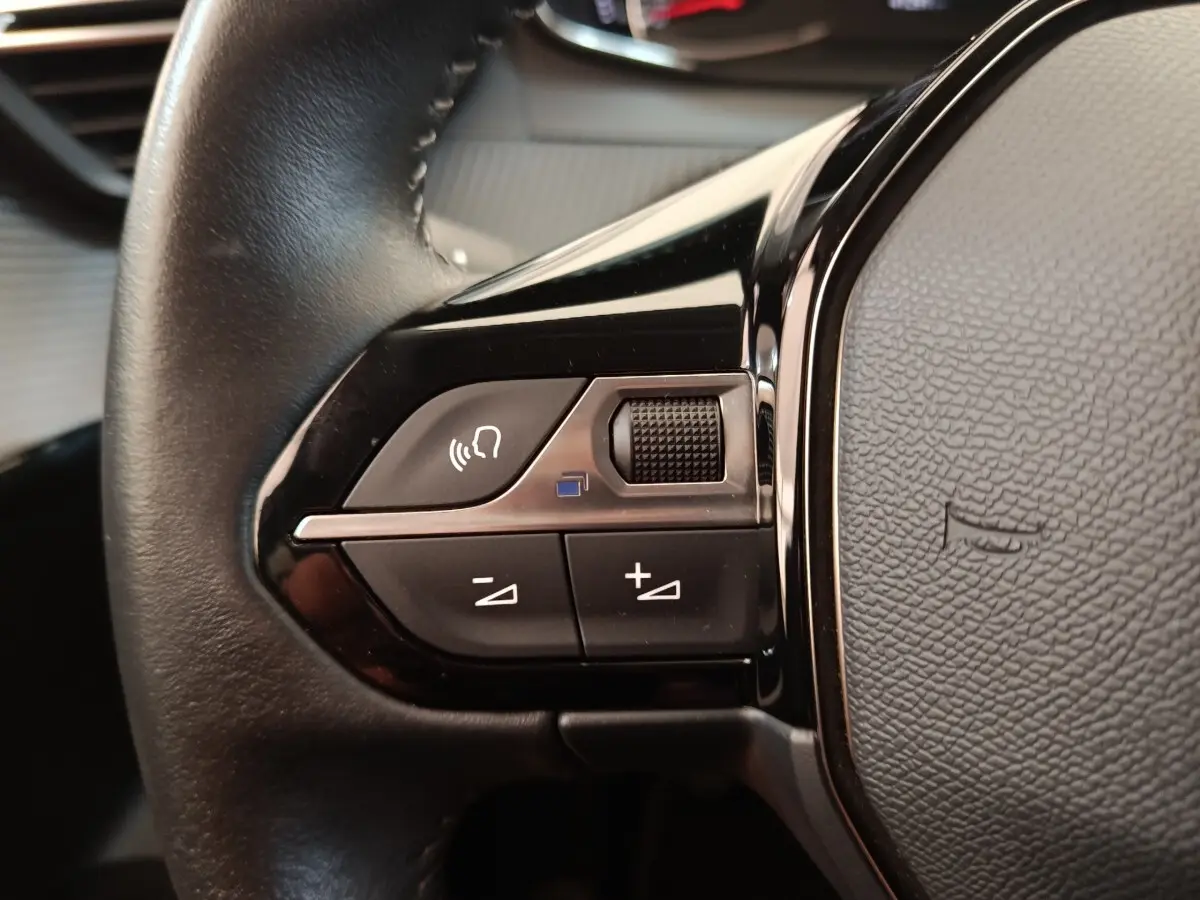Gros plan sur le volant cuir noir de la Peugeot 208 PureTech 100, avec commandes multifonctions visibles.