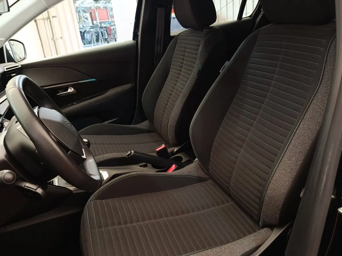 Vue intérieure côté conducteur de la Peugeot 208 PureTech 100 S&S Style 2022 avec sièges tissu noirs et volant cuir multifonctions.