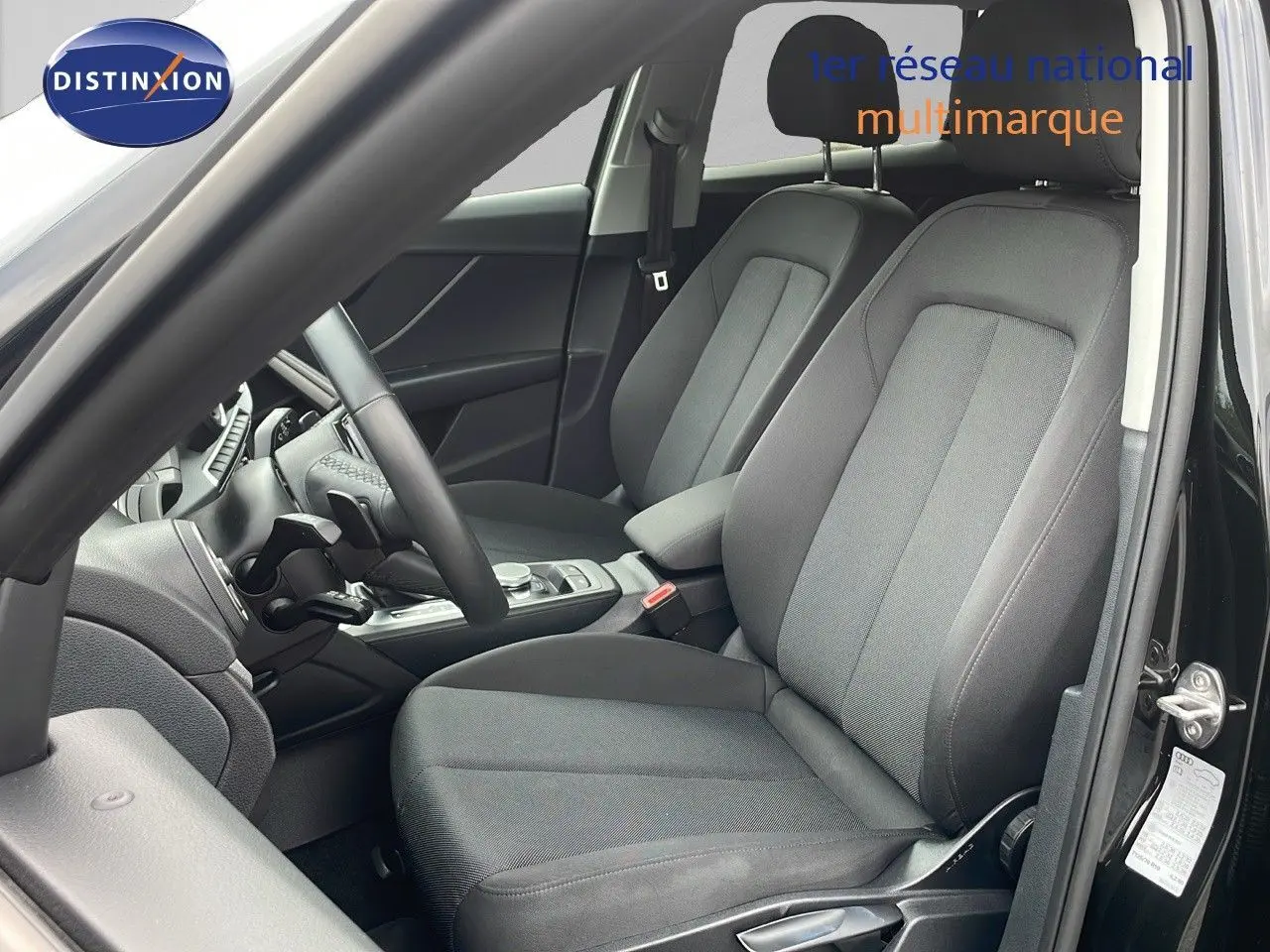 Vue intérieure côté conducteur de l'Audi Q2 35 TFSI 2023 avec sièges tissu gris et tableau de bord noir.