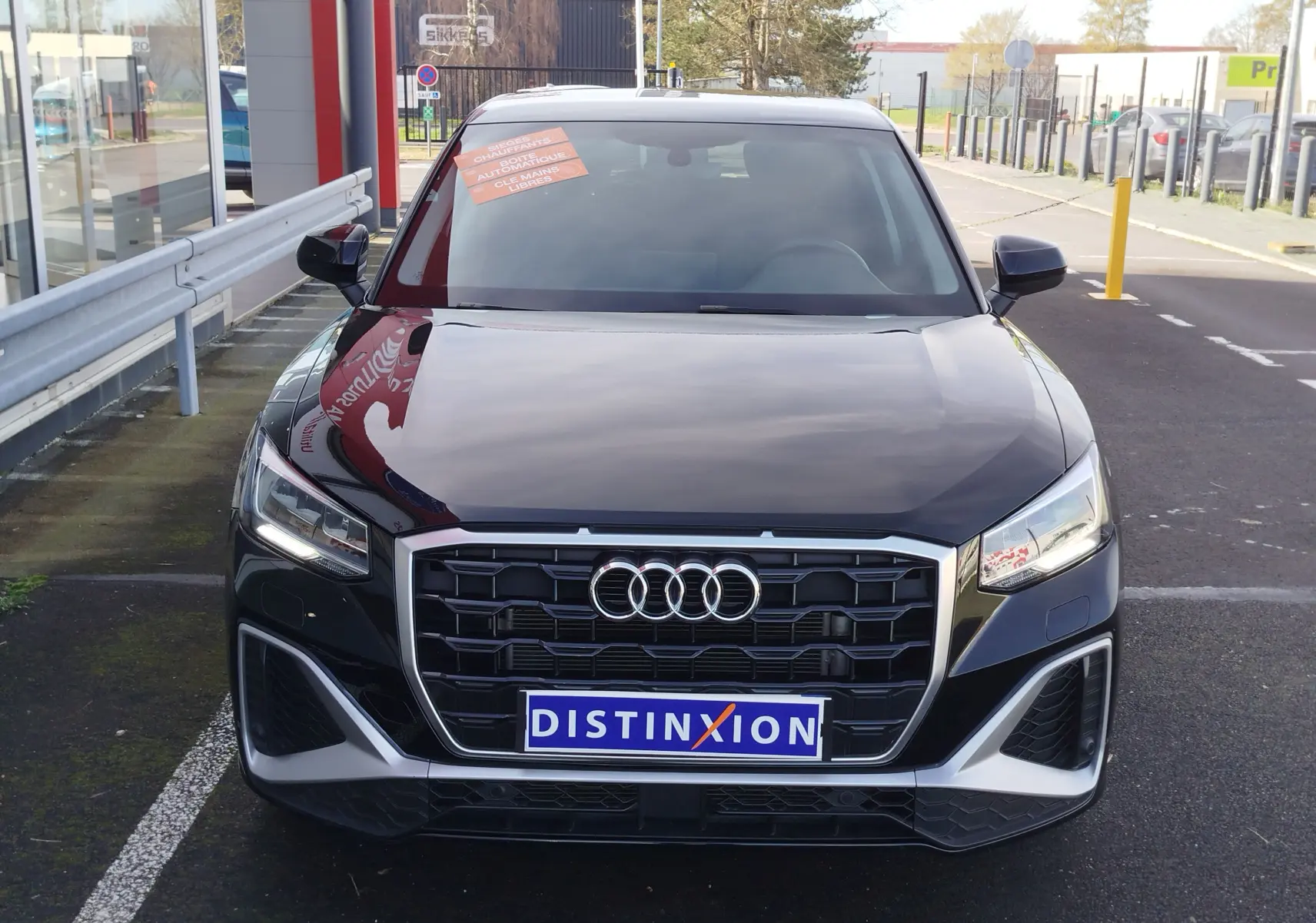 Audi Q2 35 TFSI S-Line noir mito metal, vue de face, calandre hexagonale et phares LED allumés.