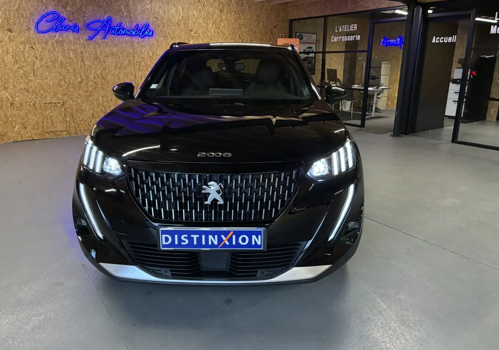 Vue de face d'un Peugeot 2008 noir 2020 avec phares allumés et calandre distinctive dans un showroom.