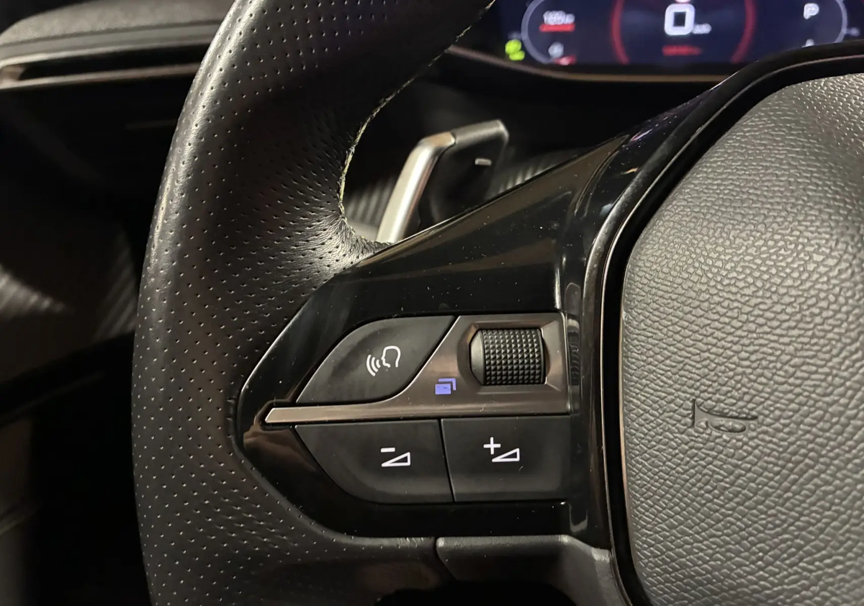 Gros plan sur la partie gauche du volant noir perforé du Peugeot 2008 1.5 BlueHDi 130 GT Line de 2020 avec commandes intégrées.