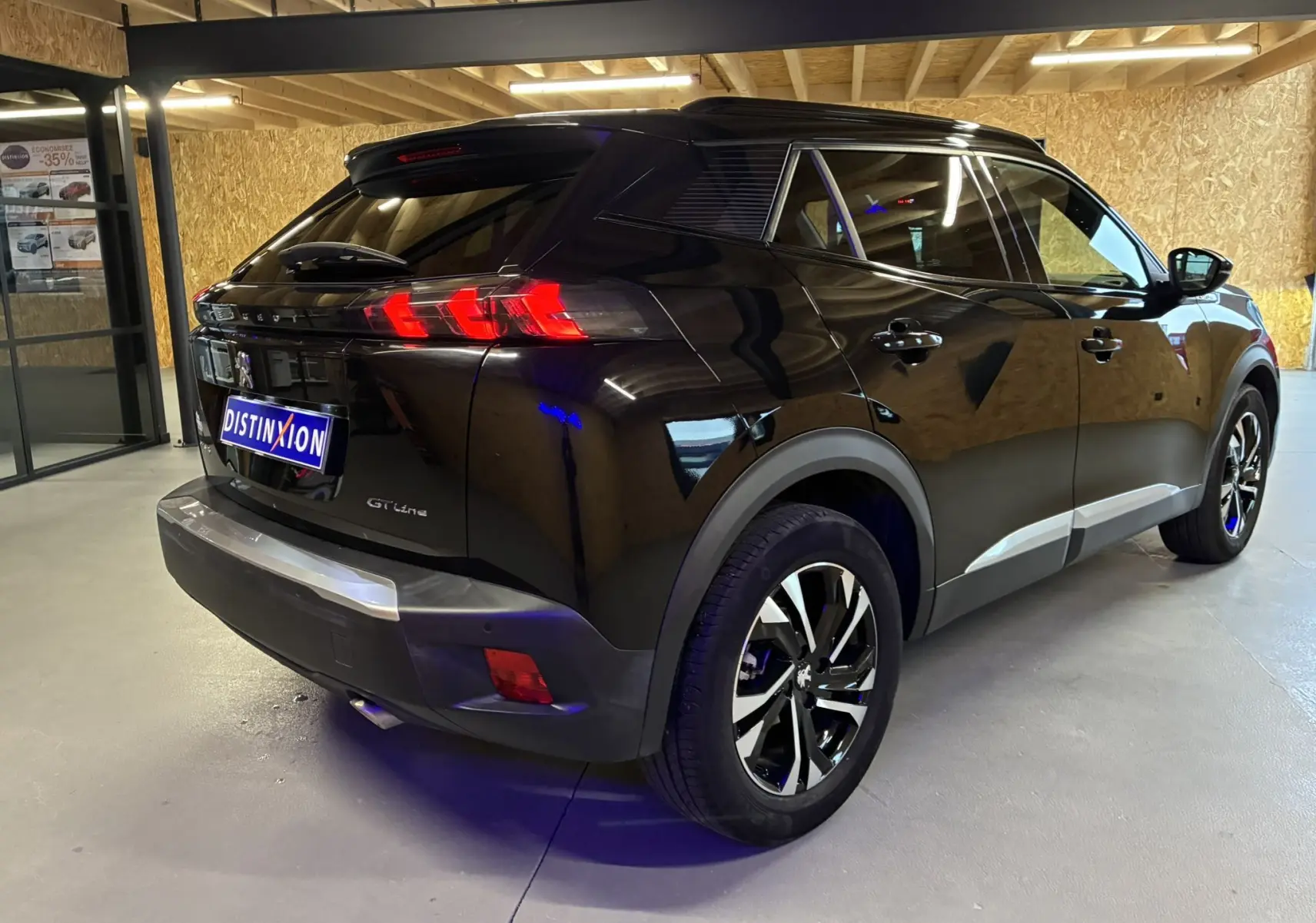 Vue 3/4 arrière droite d'un Peugeot 2008 noir GT Line 2020 avec feux arrière allumés et jantes bi-ton en intérieur showroom.