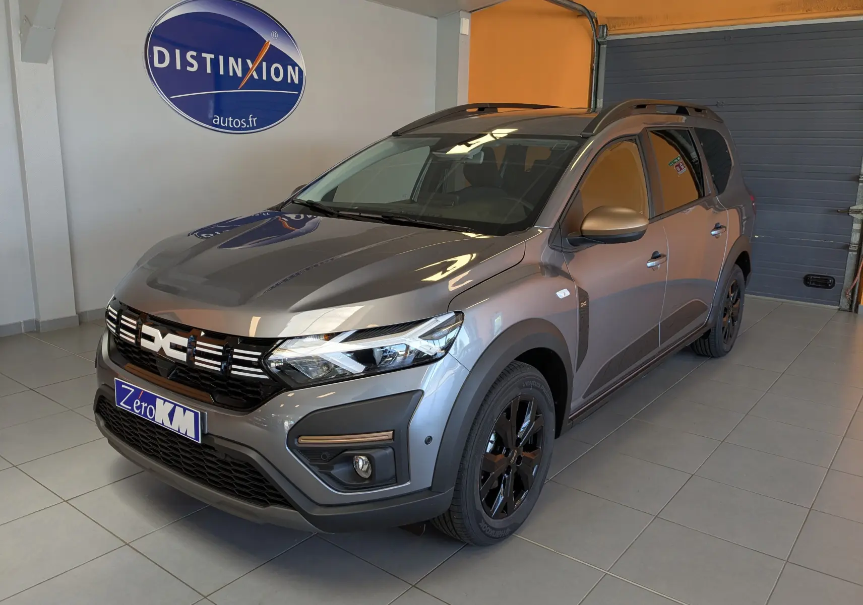 Vue 3/4 avant droite d'un Dacia Jogger gris schiste métallisé avec jantes noires et toit ouvrant en intérieur showroom.