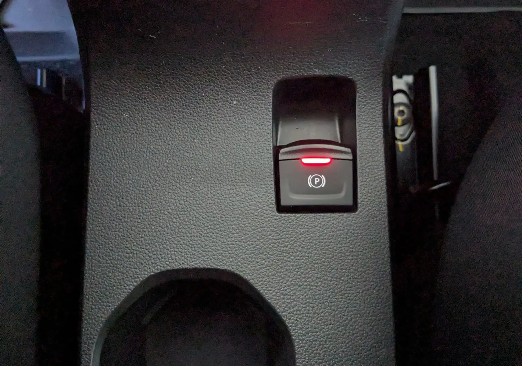 Gros plan sur le bouton de frein à main électronique allumé, sur la console centrale intérieure du Dacia Jogger gris schiste.