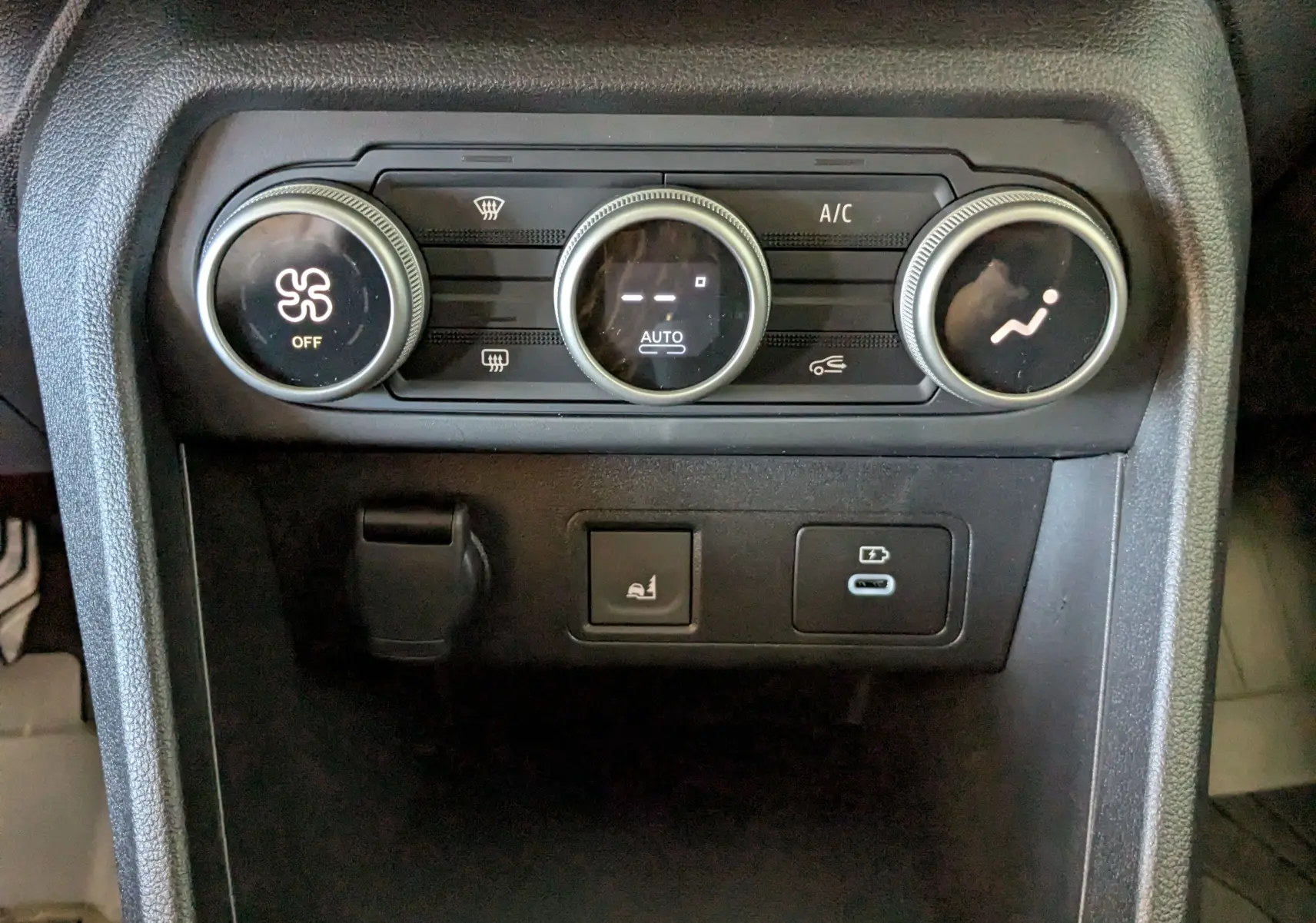 Gros plan sur la console centrale noire du Dacia Jogger 2026, avec commandes de climatisation et prises USB visibles.