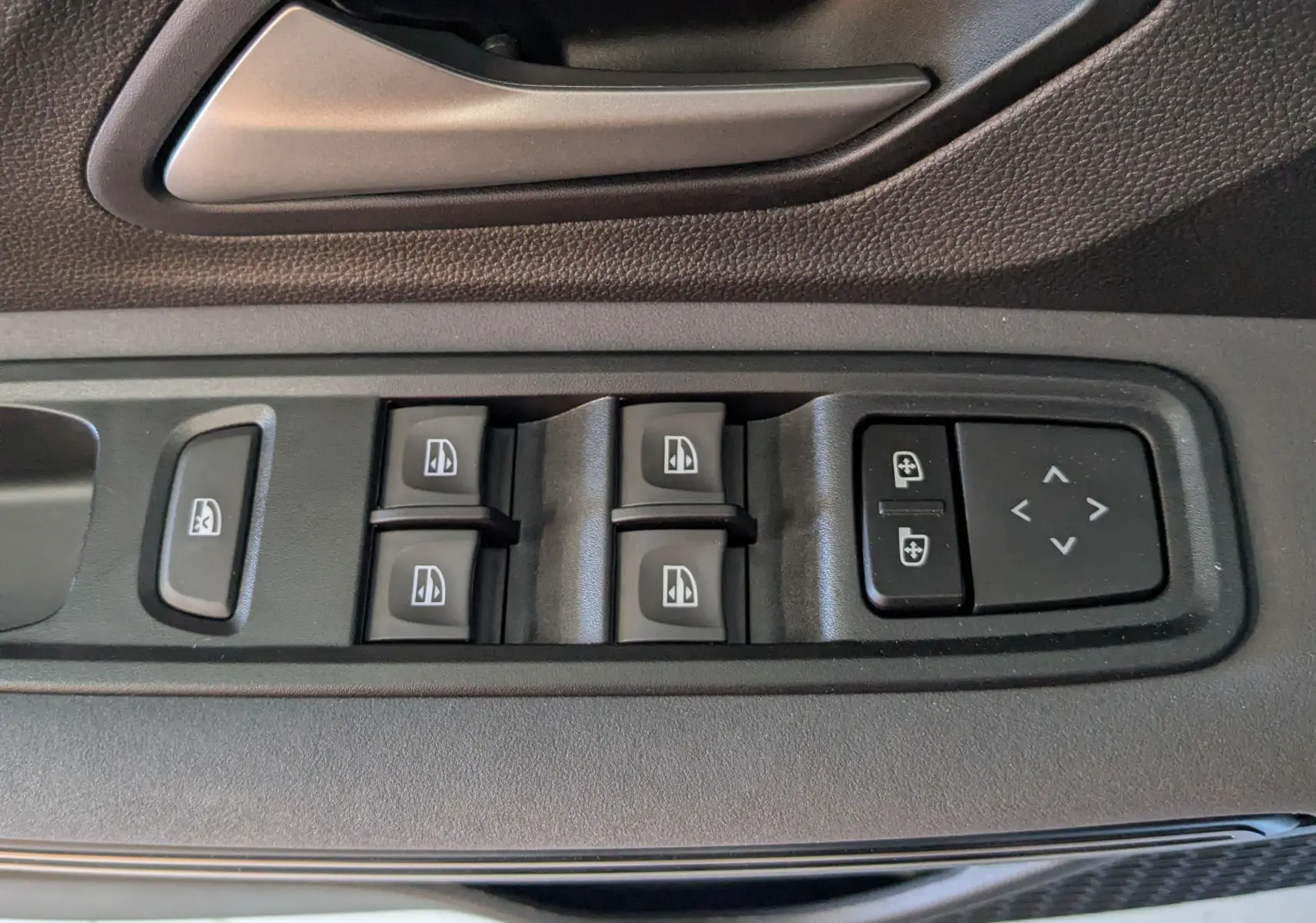 Gros plan sur les commandes des vitres et rétroviseurs sur la portière intérieure noire d'une Dacia Jogger 2026.