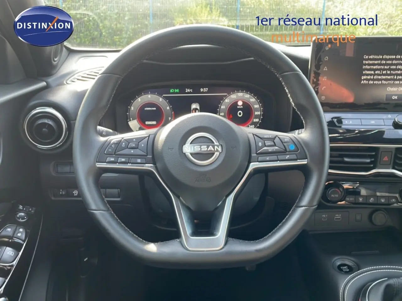 Vue intérieure centrée sur le volant cuir noir du Nissan Juke 2025, avec tableau de bord numérique et écran tactile visible.