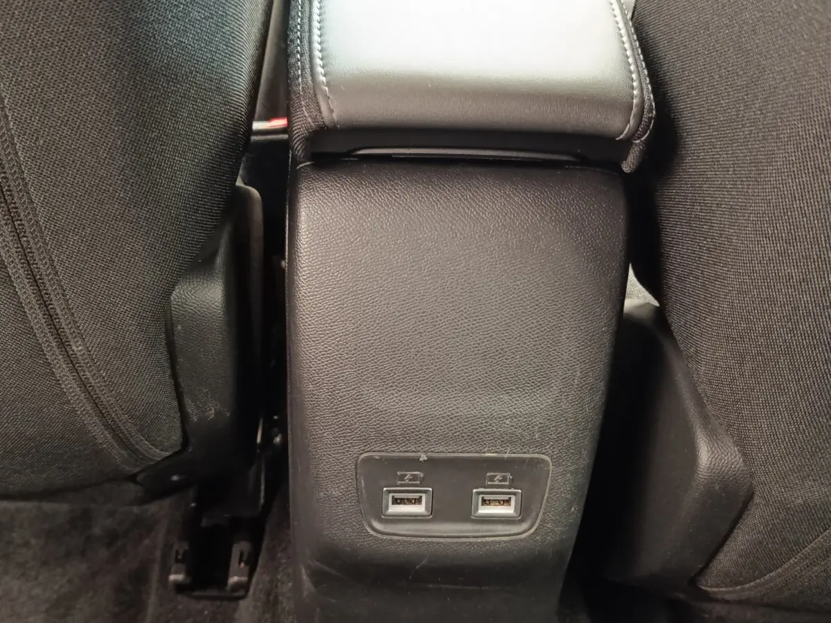 Gros plan sur la console centrale arrière noire avec deux ports USB entre les sièges tissu noirs du Peugeot E-2008 électrique.