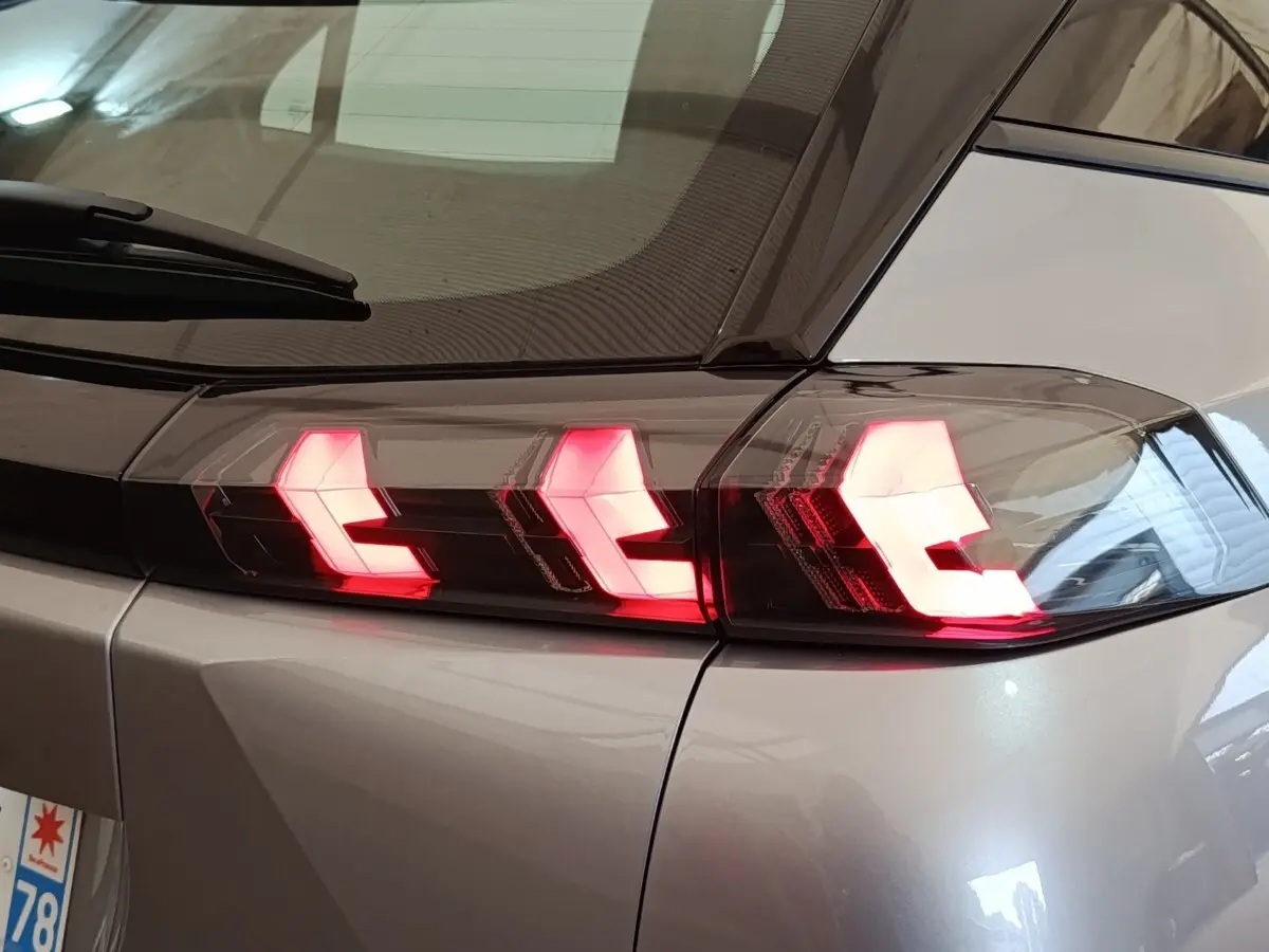 Gros plan sur le feu arrière droit allumé d’un Peugeot E-2008 électrique gris clair 2023.