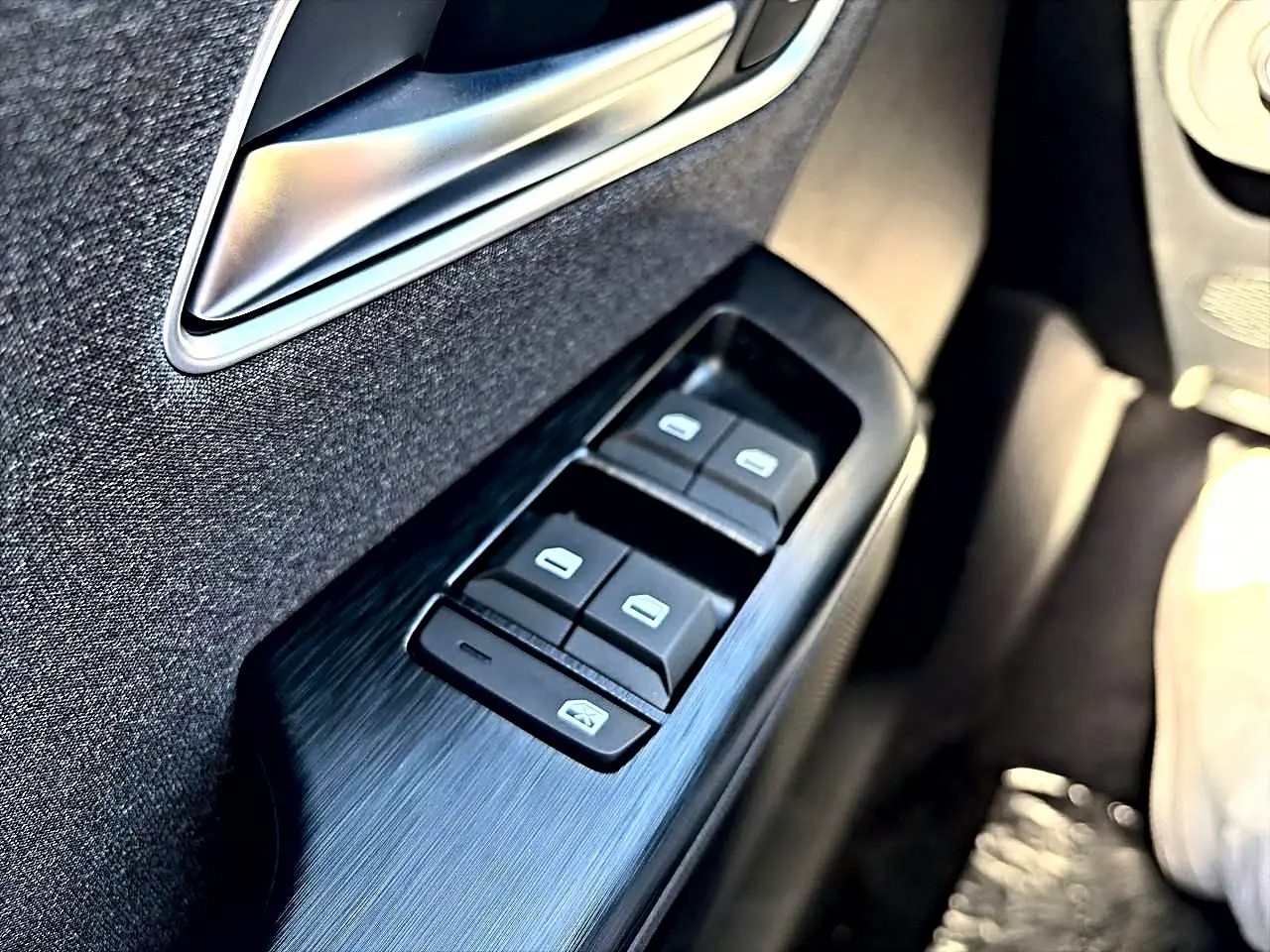 Gros plan sur la commande des vitres électriques côté conducteur du MG ZS hybride noir, avec poignée intérieure argentée.