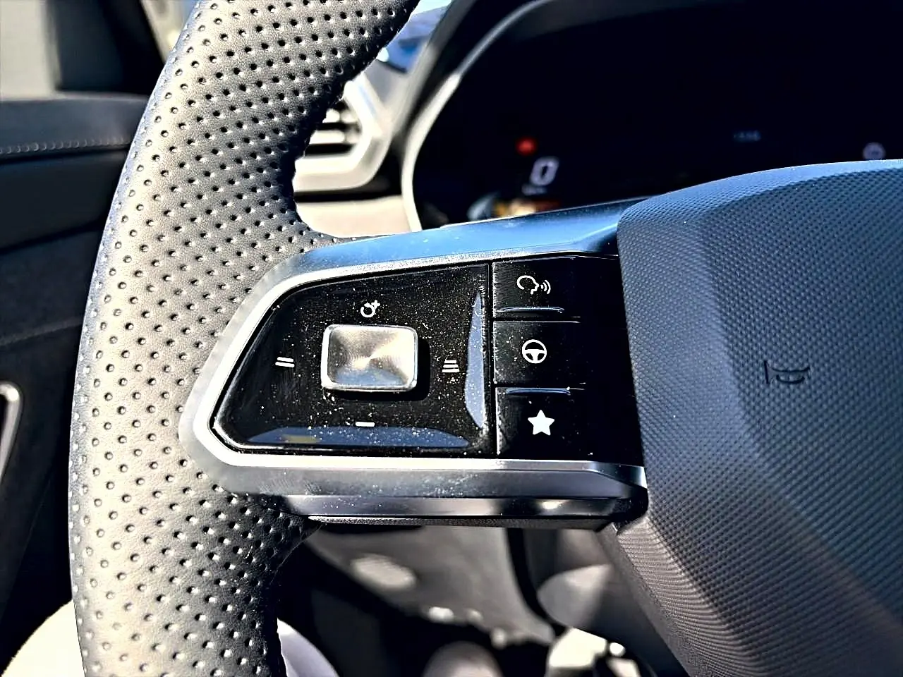Gros plan sur les commandes gauche du volant perforé noir du MG Motor ZS 1.5 hybrid 197 standard, avec boutons multifonctions.