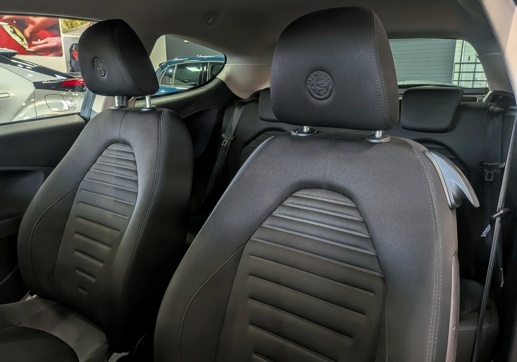 Gros plan sur les sièges avant noirs en tissu de l'Alfa Romeo MiTo 1.3 JTDm 95 CH Super de 2018 avec logo brodé sur les appuie-têtes.