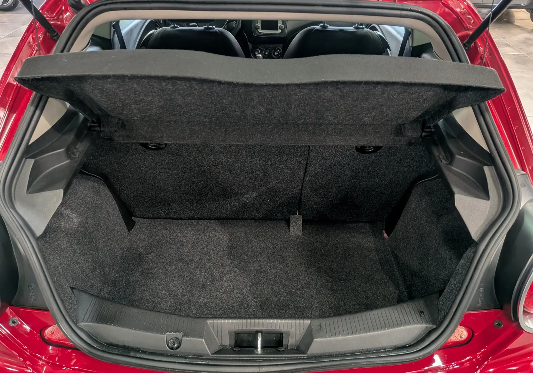 Coffre ouvert vu de l'arrière d'une Alfa Romeo MiTo rouge Alfa, intérieur de coffre en tissu noir.