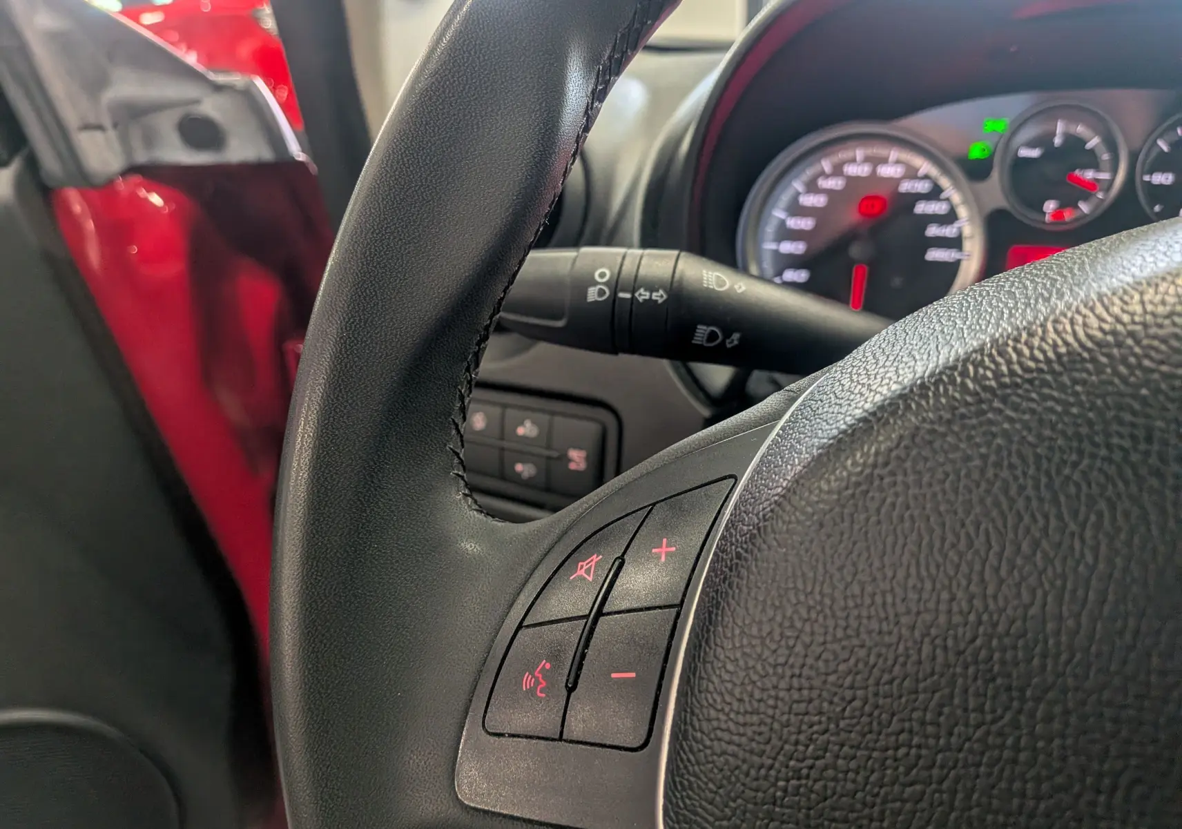 Gros plan sur le volant noir de l'Alfa Romeo MiTo rouge Alfa, avec tableau de bord et commandes au volant visibles.